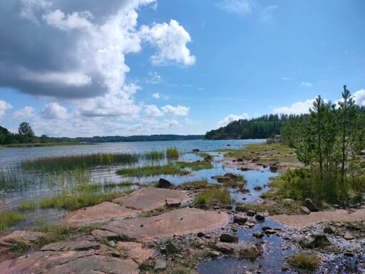 A hiking photo with a lot going on, cliffs, water, clouds, forest, and nature in all it's splendor.