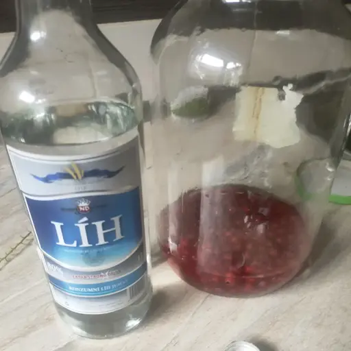 bottle of alcohol next to mason jar with red currants.