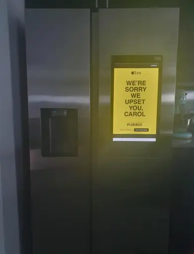 Pluribus series advertisement featuring text "We're sorry we upset you, Carol" displayed on a smart fridge's screen