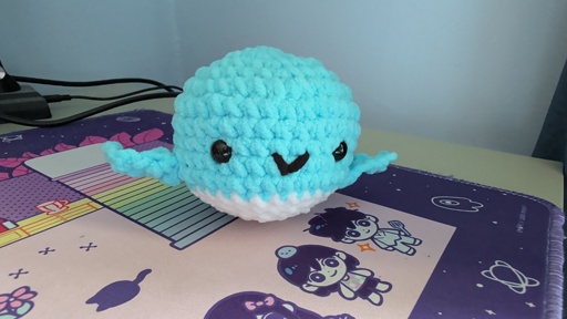 Bright blue and white small crocheted whale, with black eyes and a v-shaped smile made from black yarn