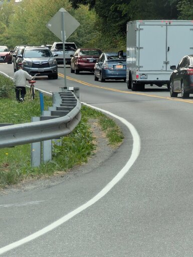 A narrow walking path created via frequent use next to a road where it crosses a ravine
