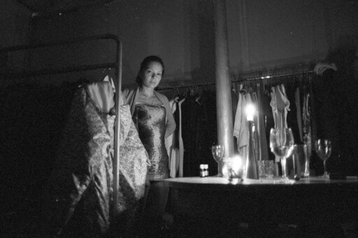A woman is standing in between some racks with clothes, it seems to be womens design clothes. The photo is black and white.
