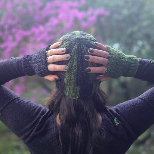 A photograph of someone wearing a matching set of black and green beanie and mittens.
